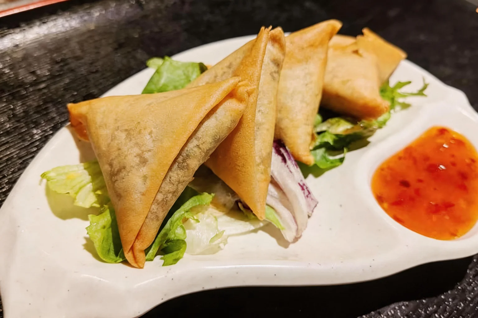 Samoussas au bœuf sur une assiette blanche, salade et sauce, plateau noir.